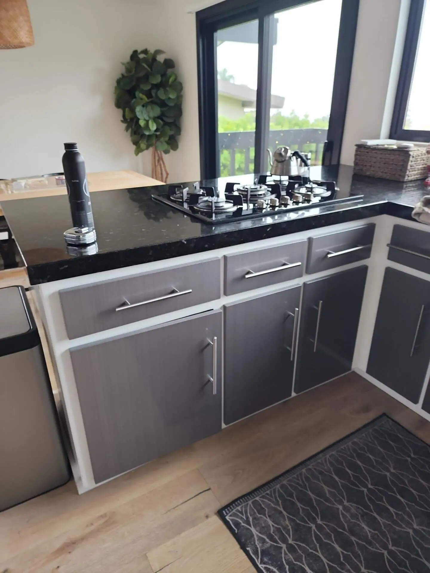 Contemporary kitchen island with grey-and-white painted cabinets and a black stone countertop, highlighting a smooth cabinet refinishing project completed by Sucro Painting Contractors.