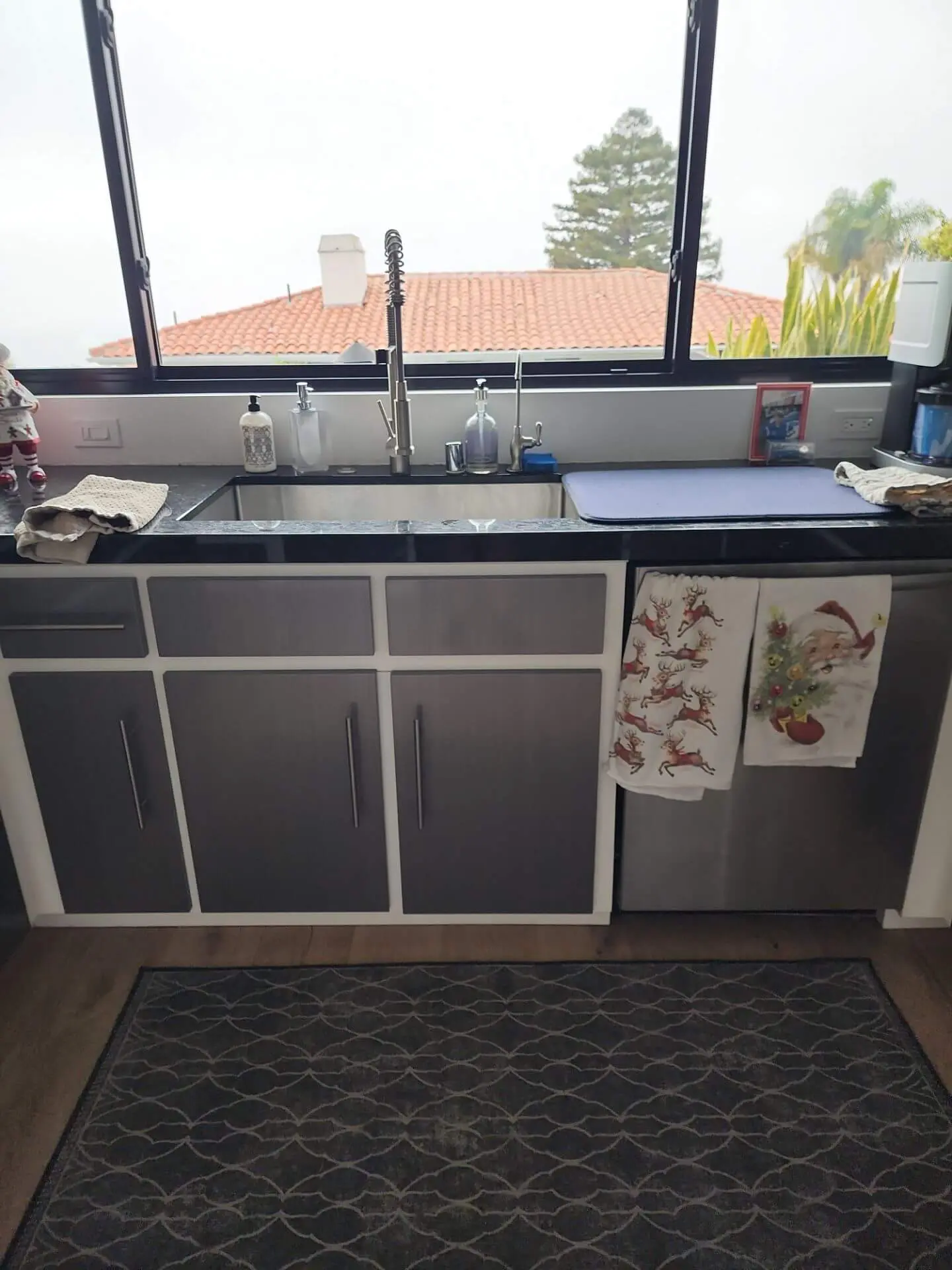 Modern kitchen sink area with grey-and-white cabinets and a sleek black countertop, showcasing a clean cabinet painting finish by Sucro Painting Contractors that refreshes the space with a contemporary look.