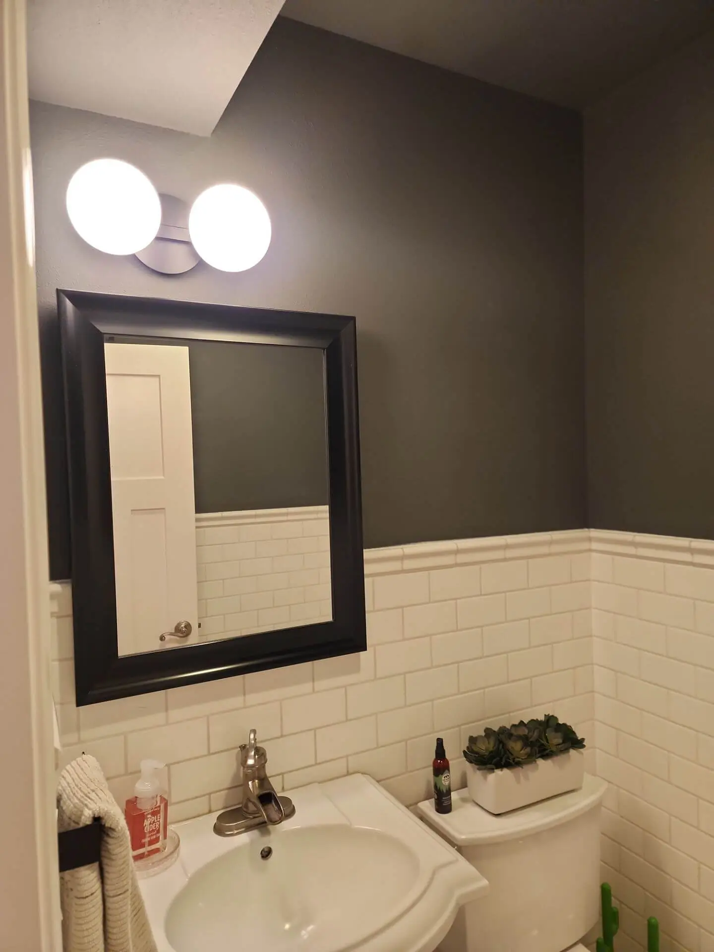 Modern bathroom with freshly painted charcoal gray walls, white subway tile wainscoting, black framed mirror, and updated vanity lighting, showcasing a clean interior painting finish by Sucro Painting Contractors.