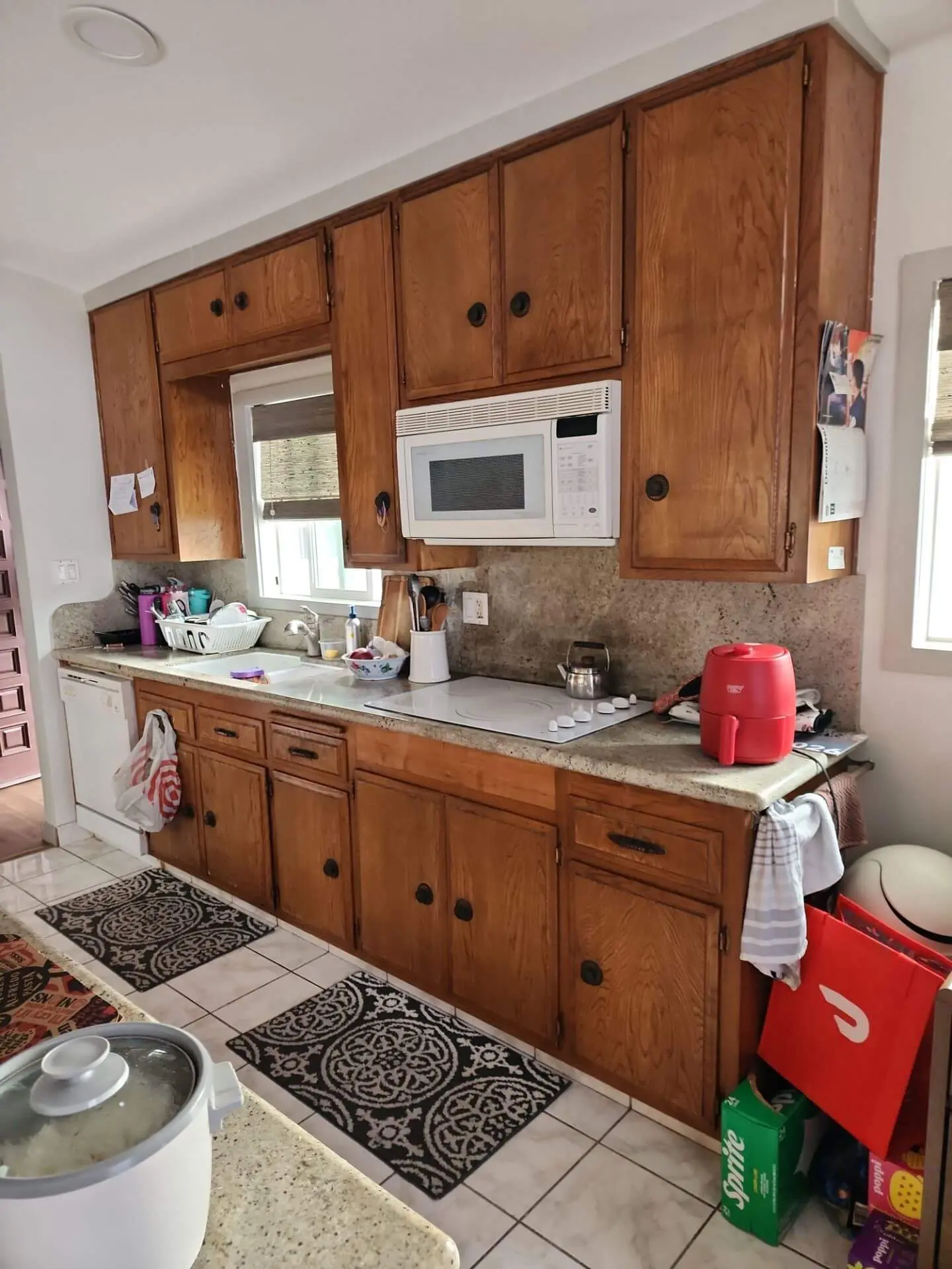Older galley-style kitchen with original oak cabinets, dated hardware, laminate countertops, and white appliances, shown before cabinet refinishing as part of a professional kitchen cabinet painting project by Sucro Painting Contractors.
