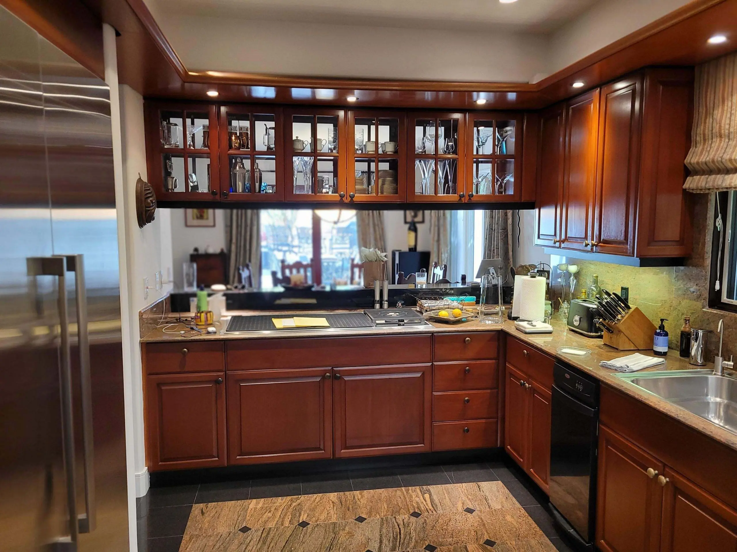 Traditional U-shaped kitchen with rich cherry wood cabinets, glass-front uppers, granite countertops, and stainless steel appliances, shown before refinishing as part of a professional cabinet painting and refinishing project by Sucro Painting Contractors.
