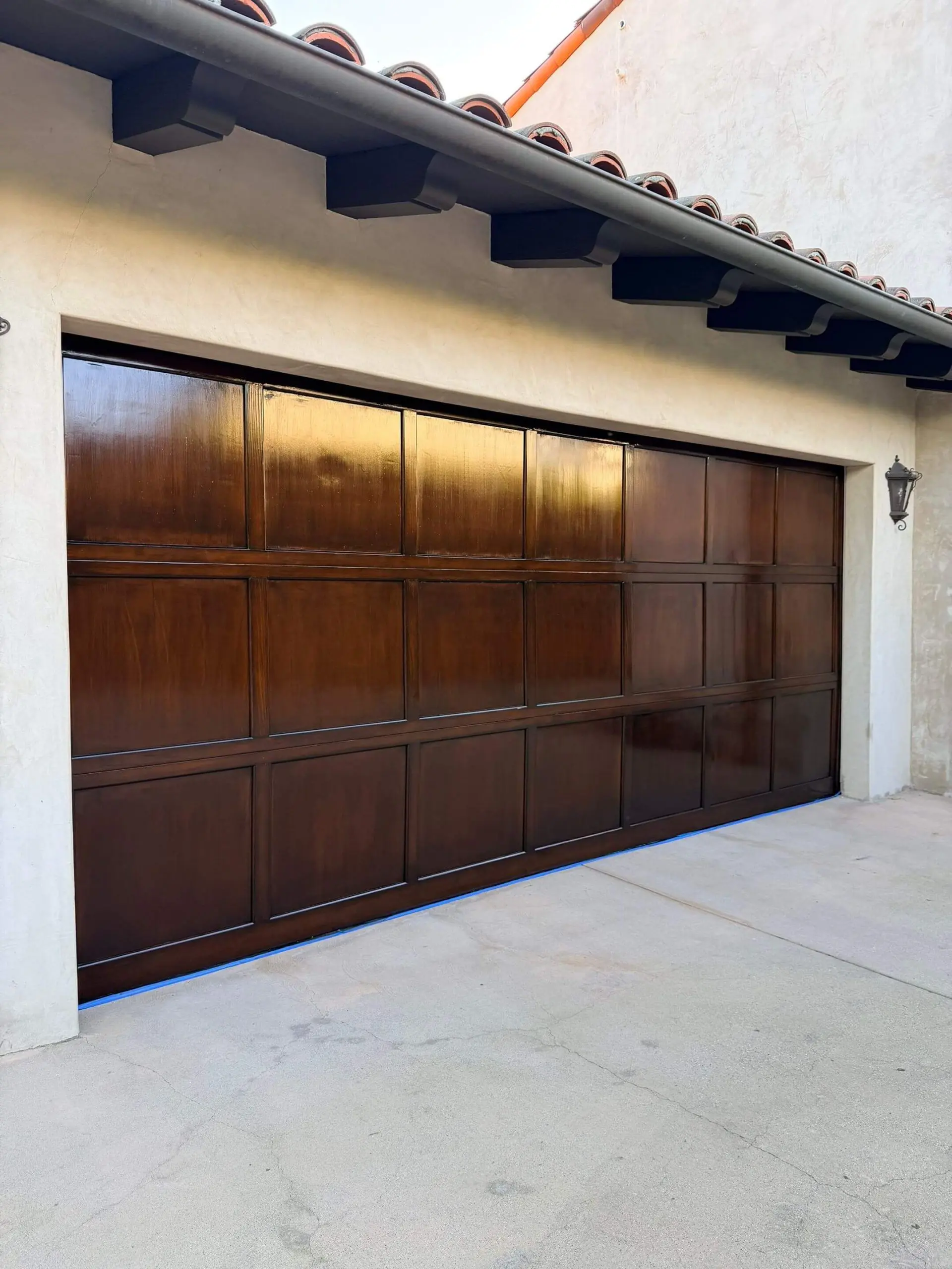 Rich dark-stained wooden garage door with a smooth, even finish, professionally refinished by Sucro Painting Contractors to enhance curb appeal and durability.