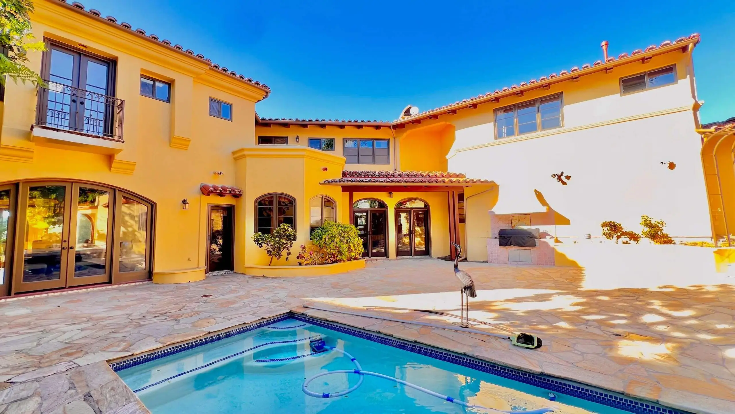 Luxury Mediterranean-style home with bright yellow exterior and courtyard pool area, showcasing smooth stucco painting completed by Sucro Painting Contractors for a bold, high-end finish.