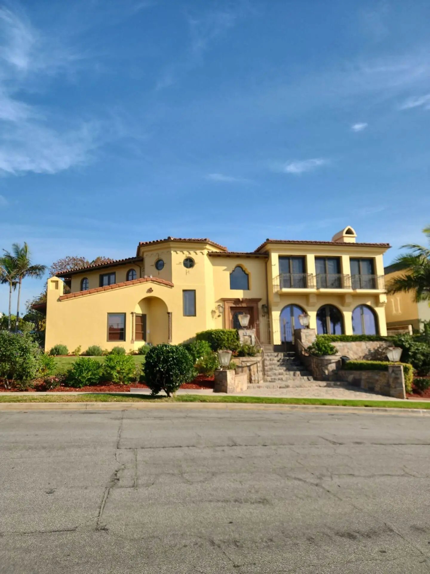Elegant Mediterranean-style home with smooth stucco exterior and warm yellow paint finish, professionally painted by Sucro Painting Contractors to enhance curb appeal and architectural details.