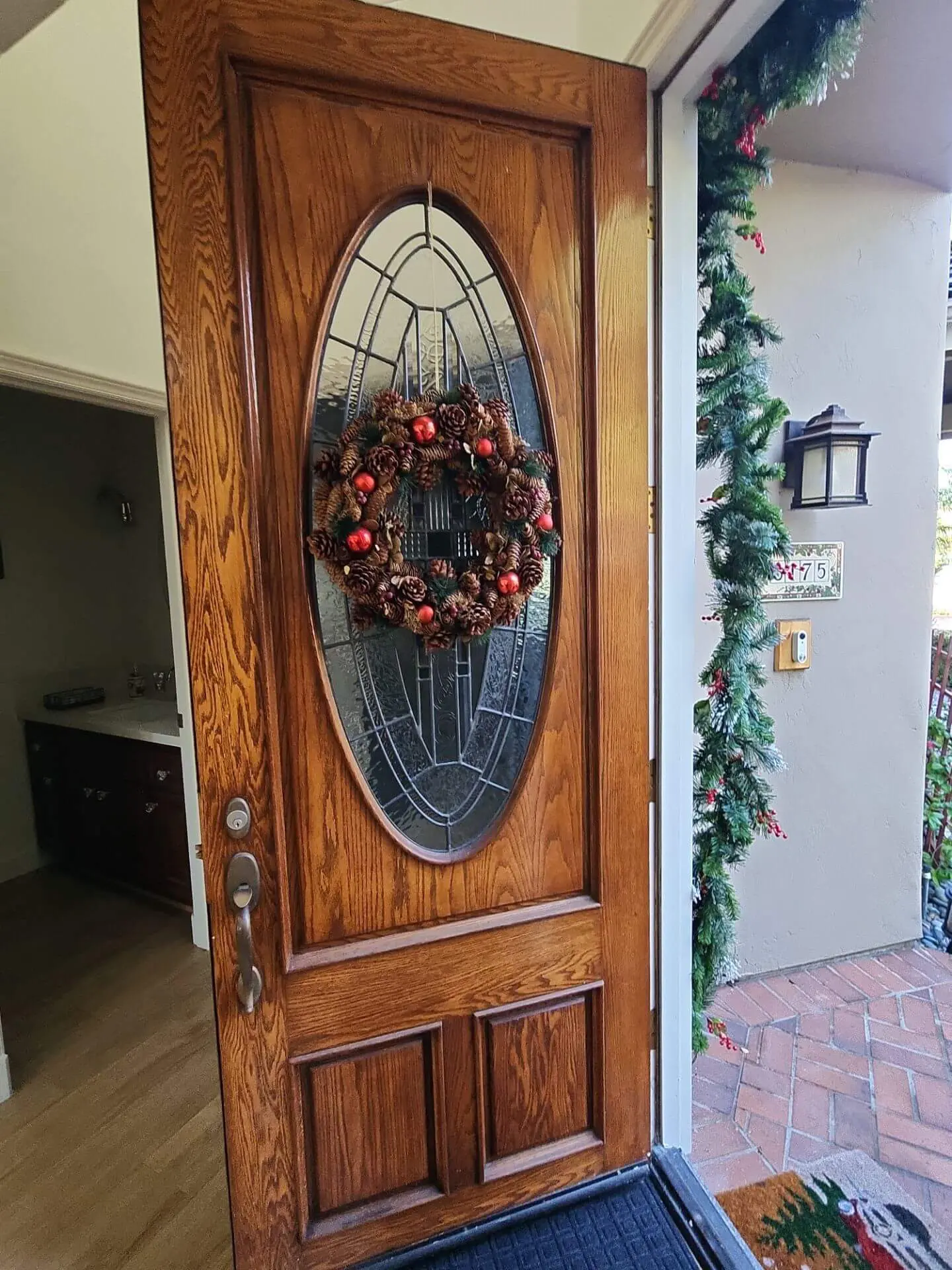 Stained wood front door with decorative glass insert and holiday wreath, professionally refinished by Sucro Painting Contractors for a warm, polished entryway.