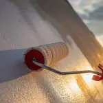 Paint roller applying white paint to a home exterior wall