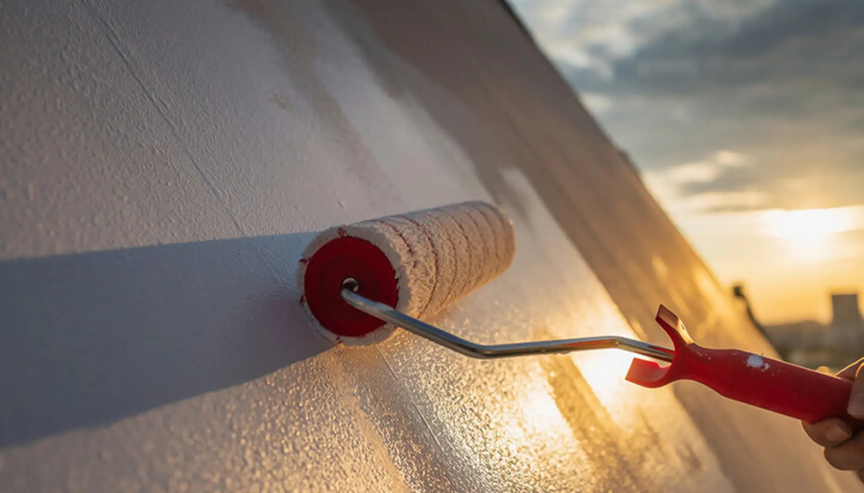 Paint roller applying white paint to a home exterior wall