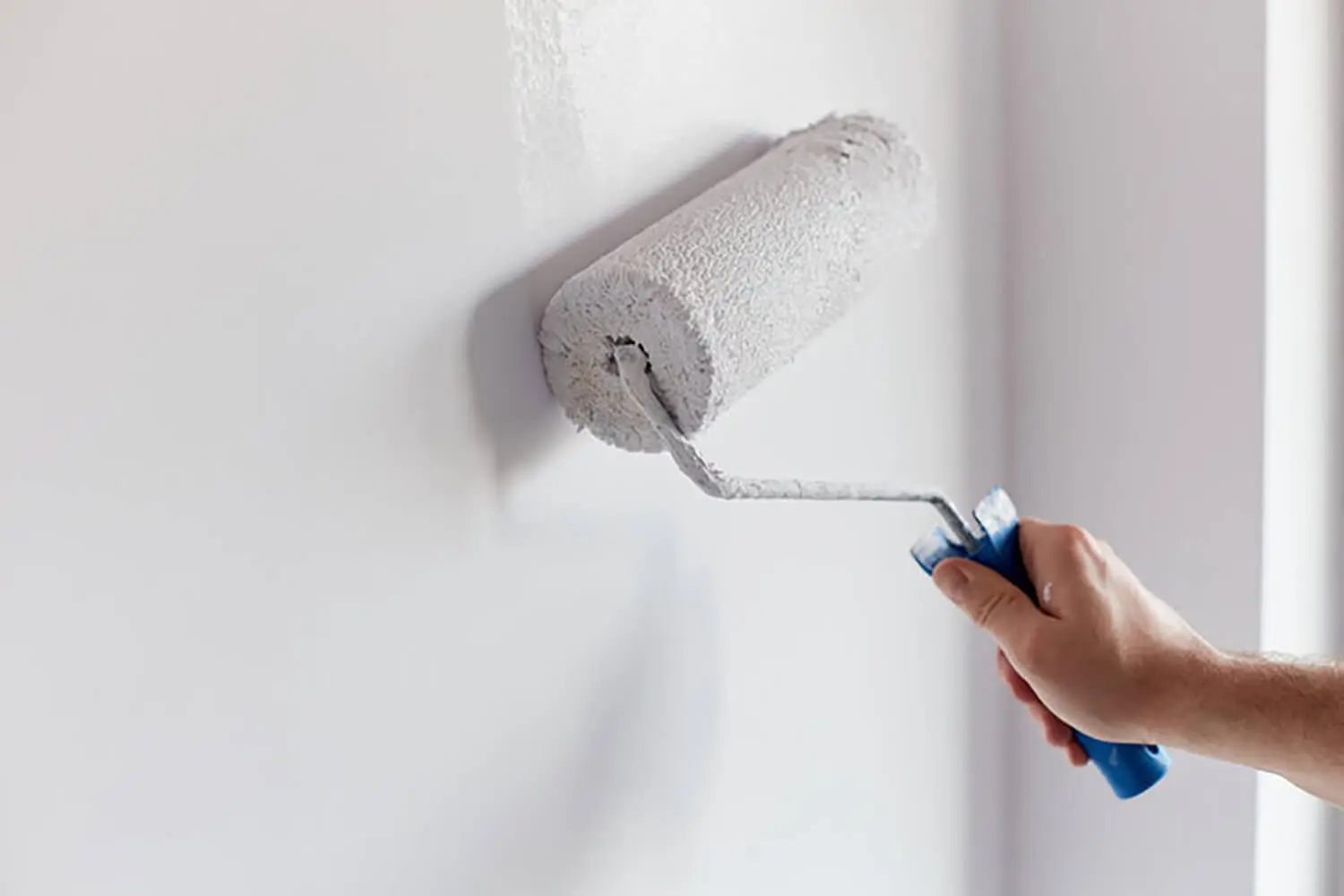 Paint roller applying white paint to an interior wall