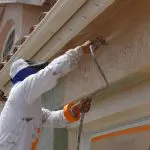Professional painter applying protective stucco coating to prevent exterior paint peeling on a South Bay home