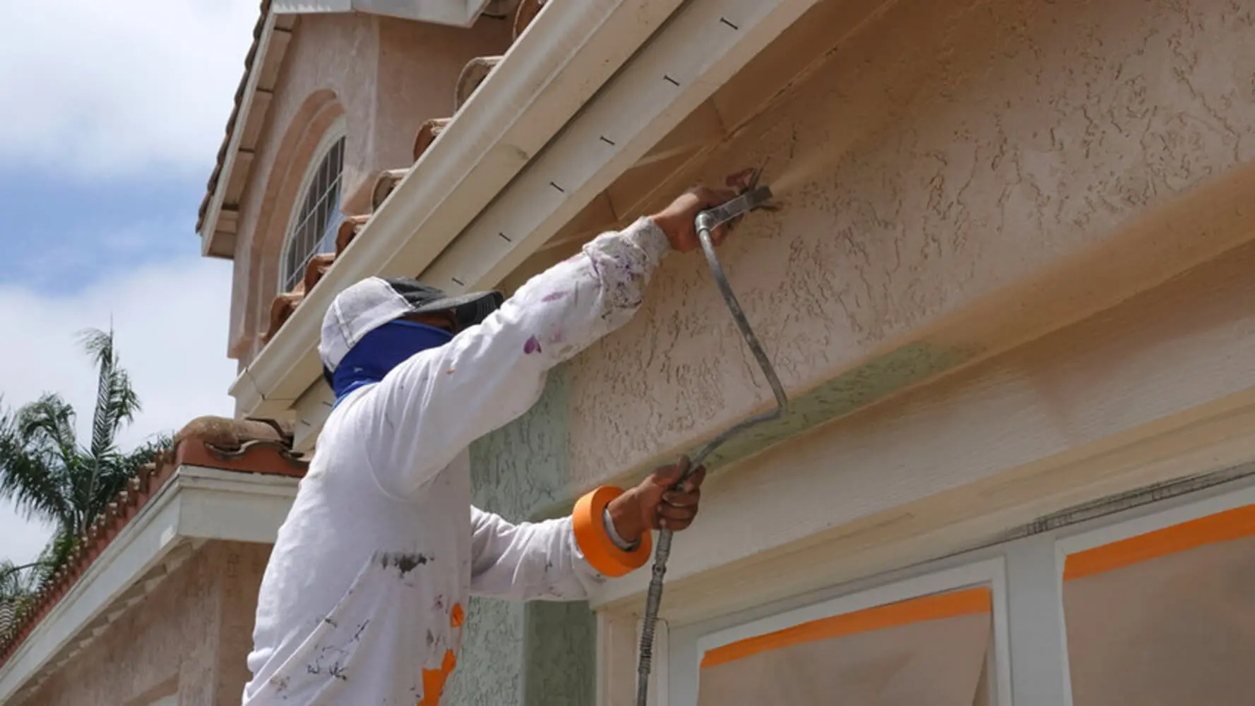 Professional painter applying protective stucco coating to prevent exterior paint peeling on a South Bay home