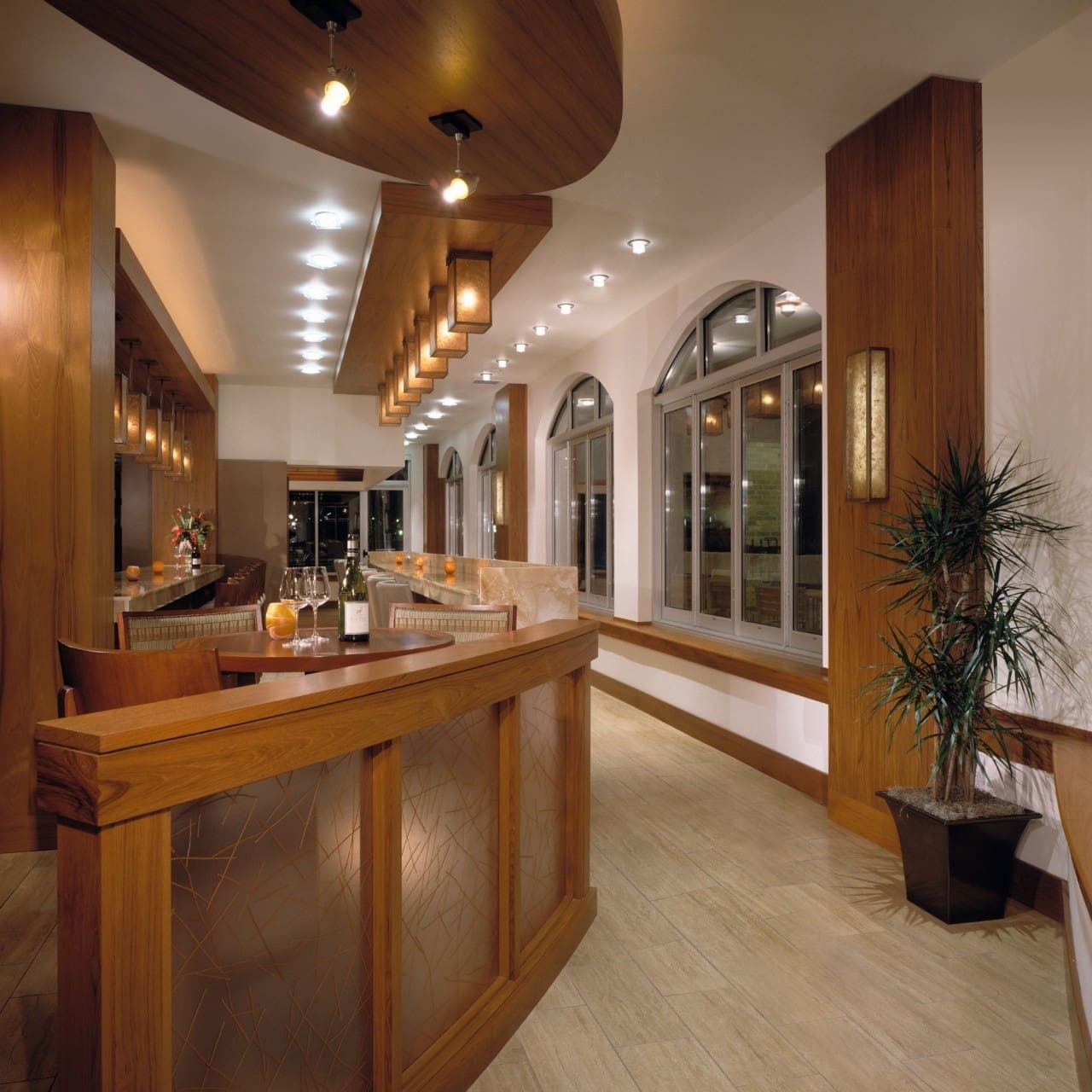 Upscale restaurant interior featuring warm Sucro Painting wall accents, custom wood paneling, arched windows, and contemporary ambient lighting over a polished bar.