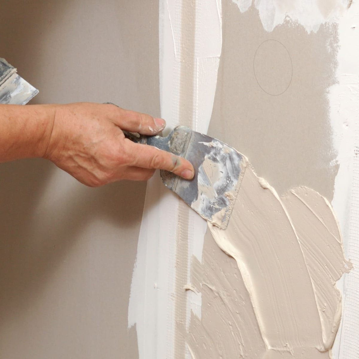 Close-up of a worker applying joint compound to a drywall seam using a putty knife during interior wall finishing.