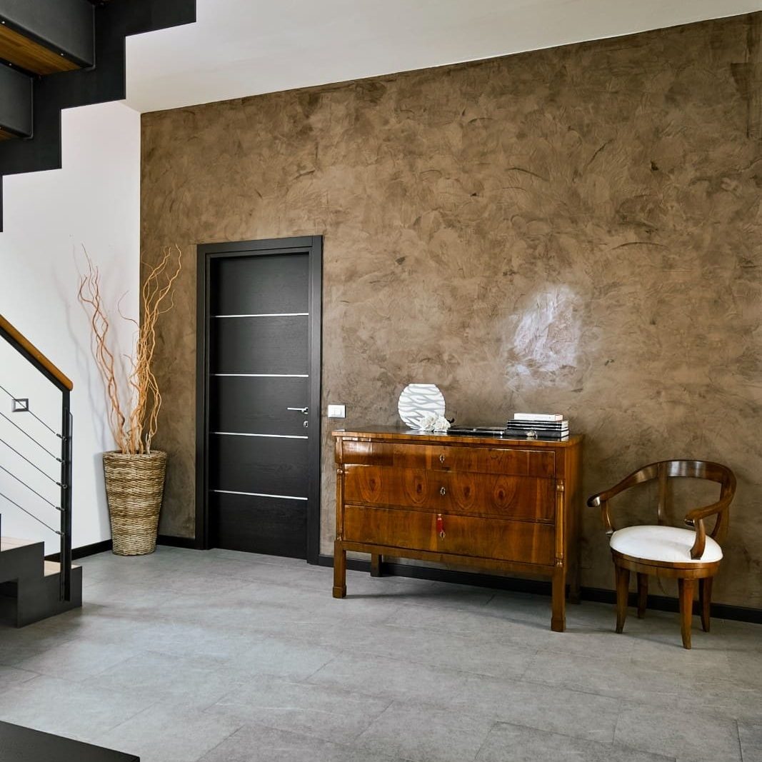 Modern interior space featuring a textured faux finish accent wall in warm brown tones, paired with a wooden console table, accent chair, and contemporary staircase design.