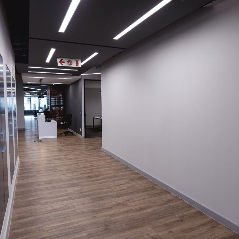 Modern commercial corridor featuring a professional Sucro Painting finish on white walls, wood-look flooring, and integrated linear LED ceiling lighting.