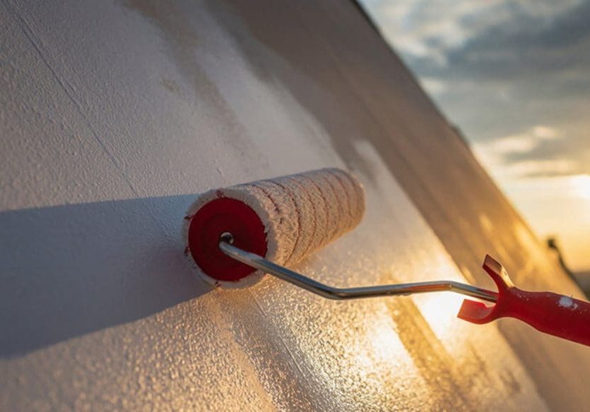 Paint roller applying white paint to a home exterior wall