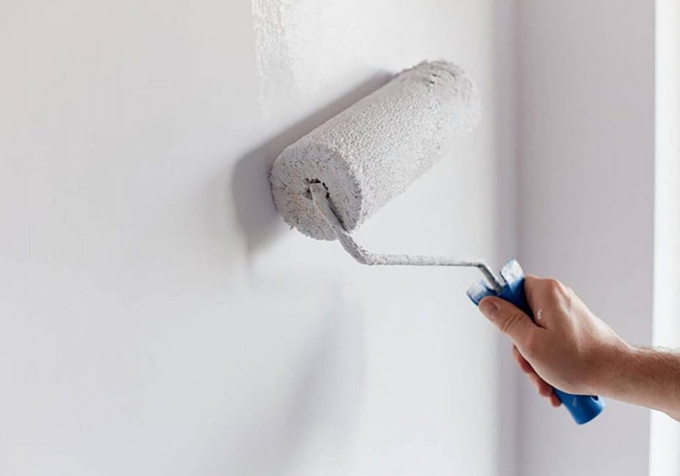 Paint roller applying white paint to an interior wall
